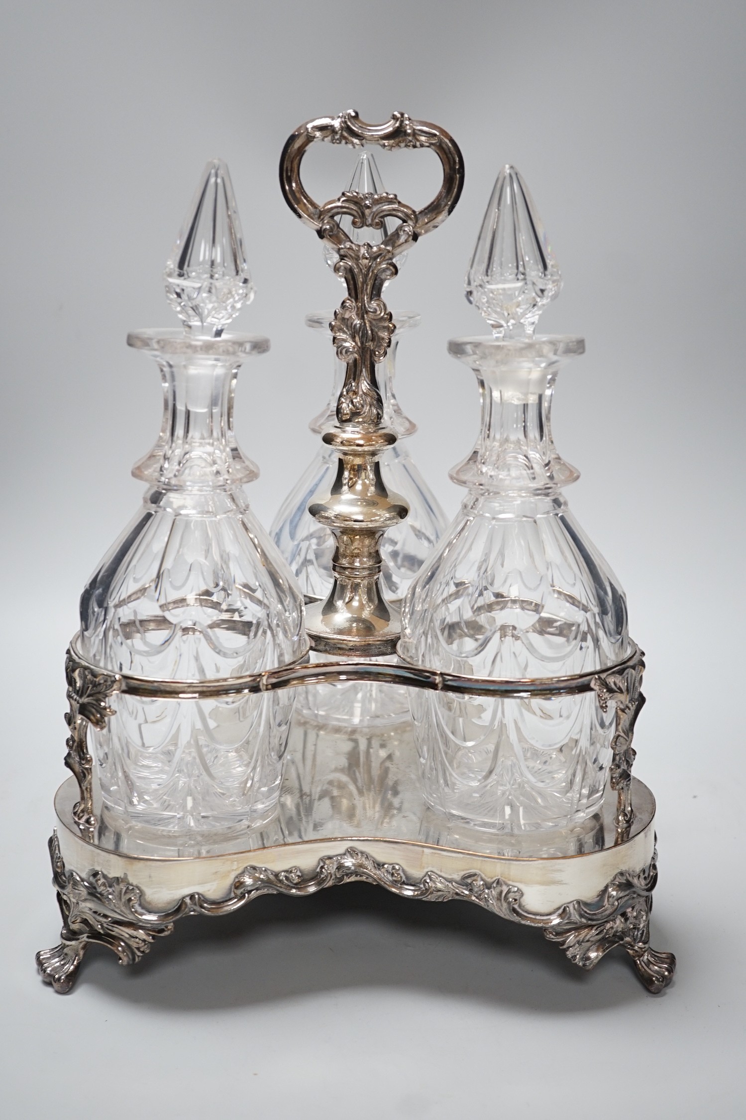 A decorative three bottle decanter set, on lion feet tripod plated stand. 37cm tall
